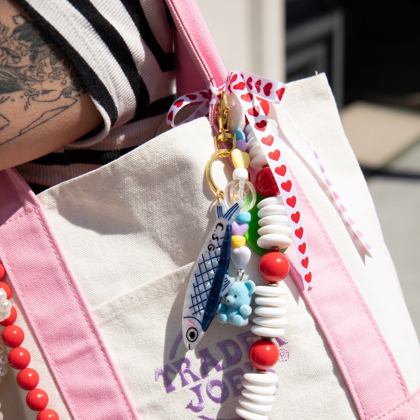 Image of a tote bag with a plastic charm in the shape of a green and red pimento olive and a blue and white anchovy with brass clasp.