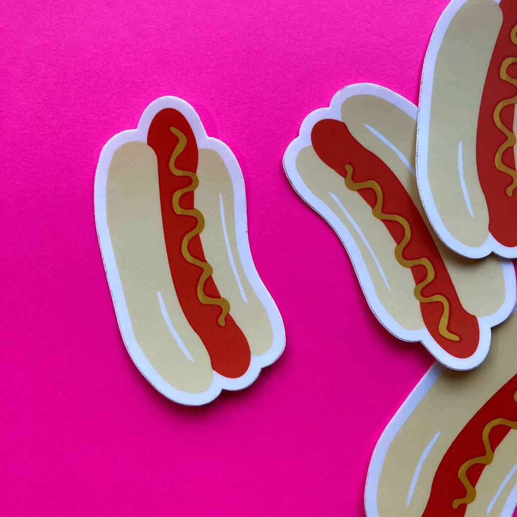 Image of a sticker shaped like a hot dog on a roll with a line of mustard on it. 