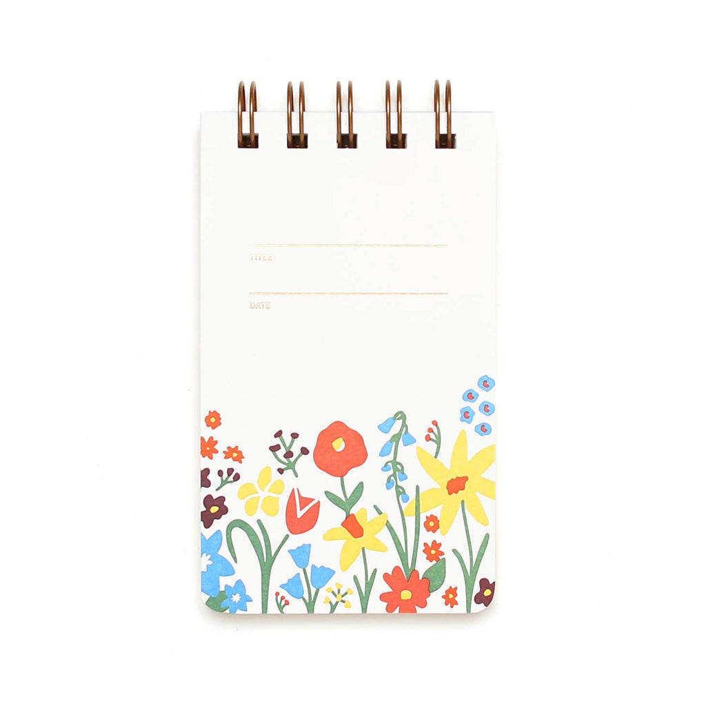 White background with garden flowers at the bottom of cover in red, yellow, blue, and green with embossed lines with embossed text says, “Title and “Date.. Brass coil binding at top. 