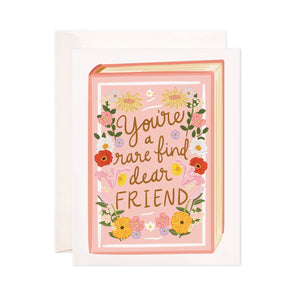 Greeting card with pale pink background in the shape of a book with yellow, blue and red flowers and brown text says, "You're a rare find dear friend". Envelope included. 