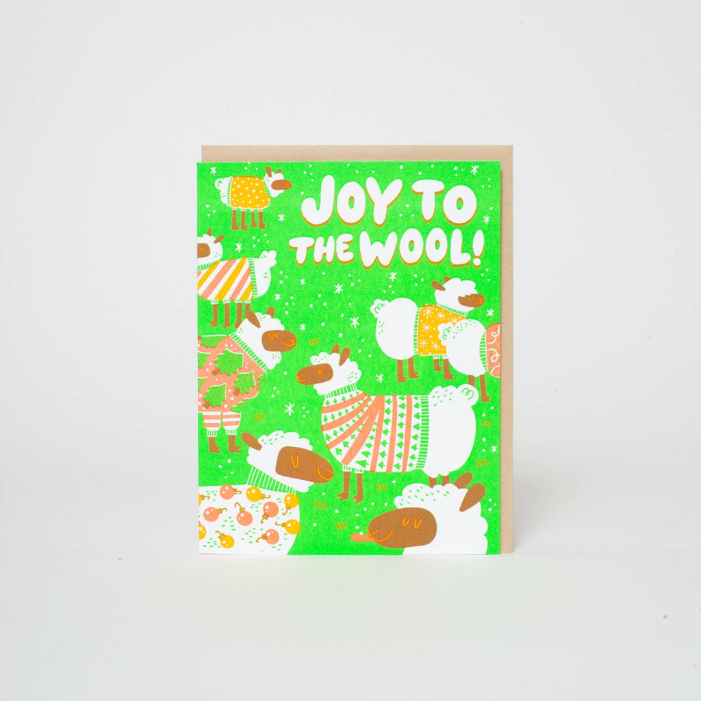 Greeting card with green background and images of sheep wearing holiday sweaters and white text says, "Joy to the wool!". Kraft envelope included. 