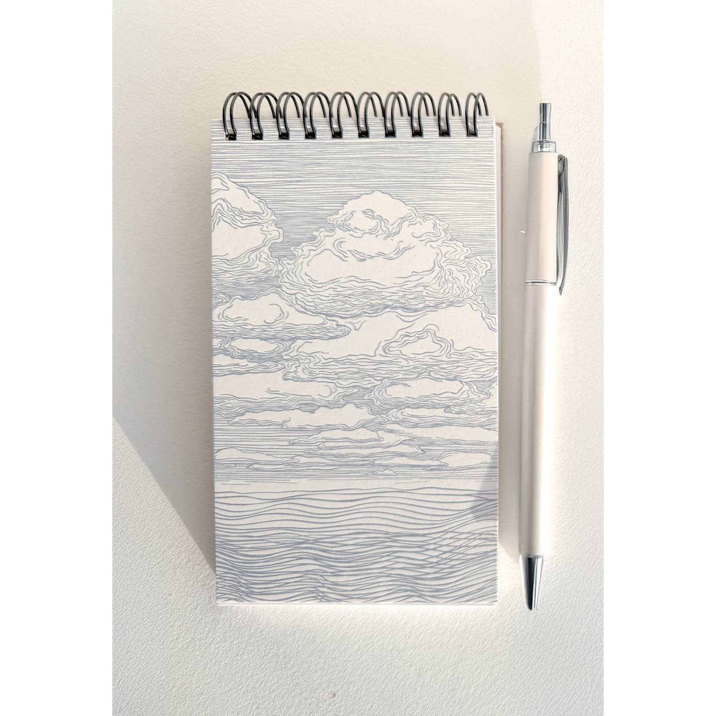 Notebook with black and white sketch of clouds on cover and coil binding at top. 