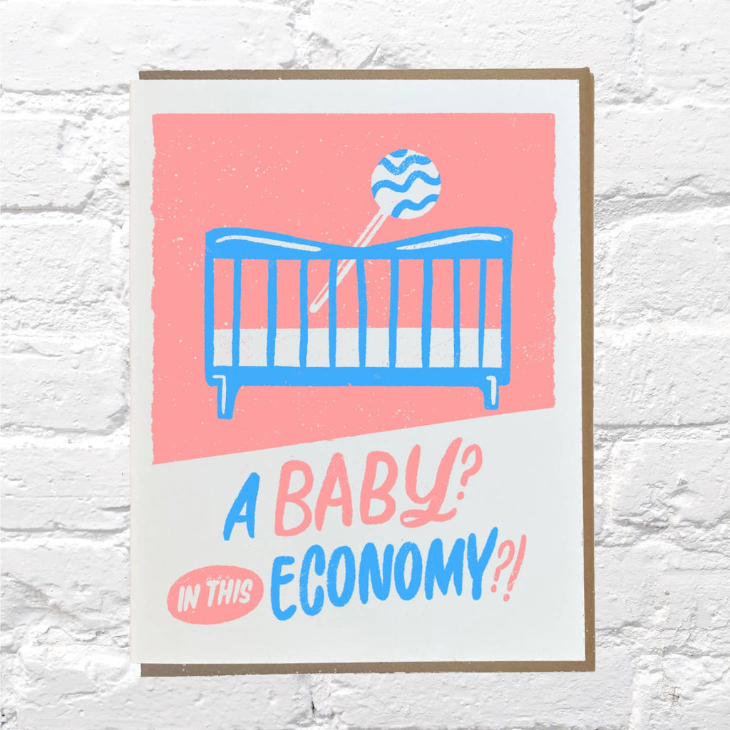 White background with image of blue crib and rattle with blue and pink text says, "A baby? In this economy?!". Kraft envelope is included. 