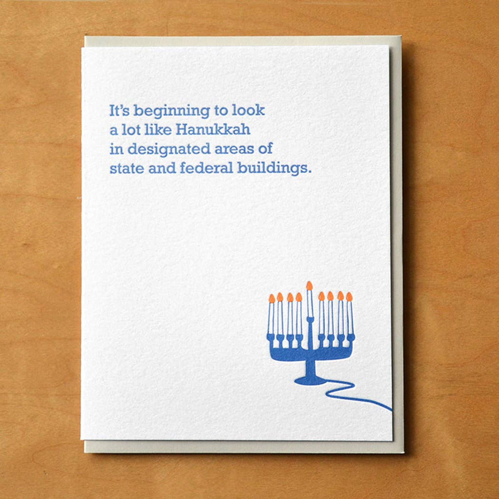 Greeting card with white background and image of a blue and white menorah with lit candles. Blue text says, "It's beginning to look a lot like Hanukkah in designated areas of state and federal buildings." Envelope included. 