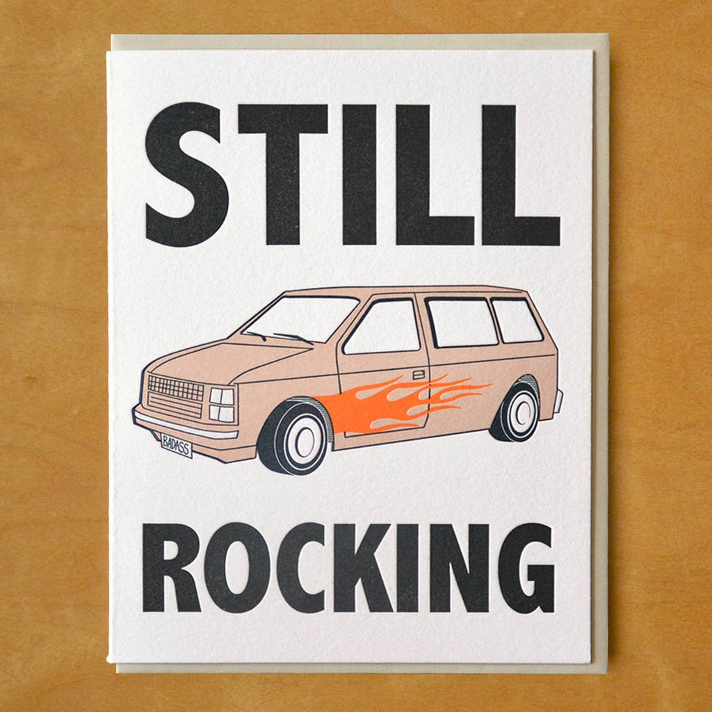 Greeting card with white background and image of a minivan with red flames on the side and black text says, "Still rocking". Tan envelope included. 