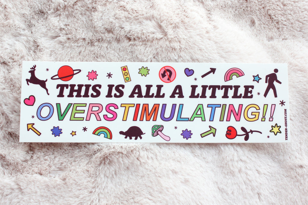 Bumper sticker with white background with images of deer, planets, rainbows, people, flowers, turtles, mushrooms, lights and black text says,"This is all a little" and rainbow text says, "Overstimulating!!". 