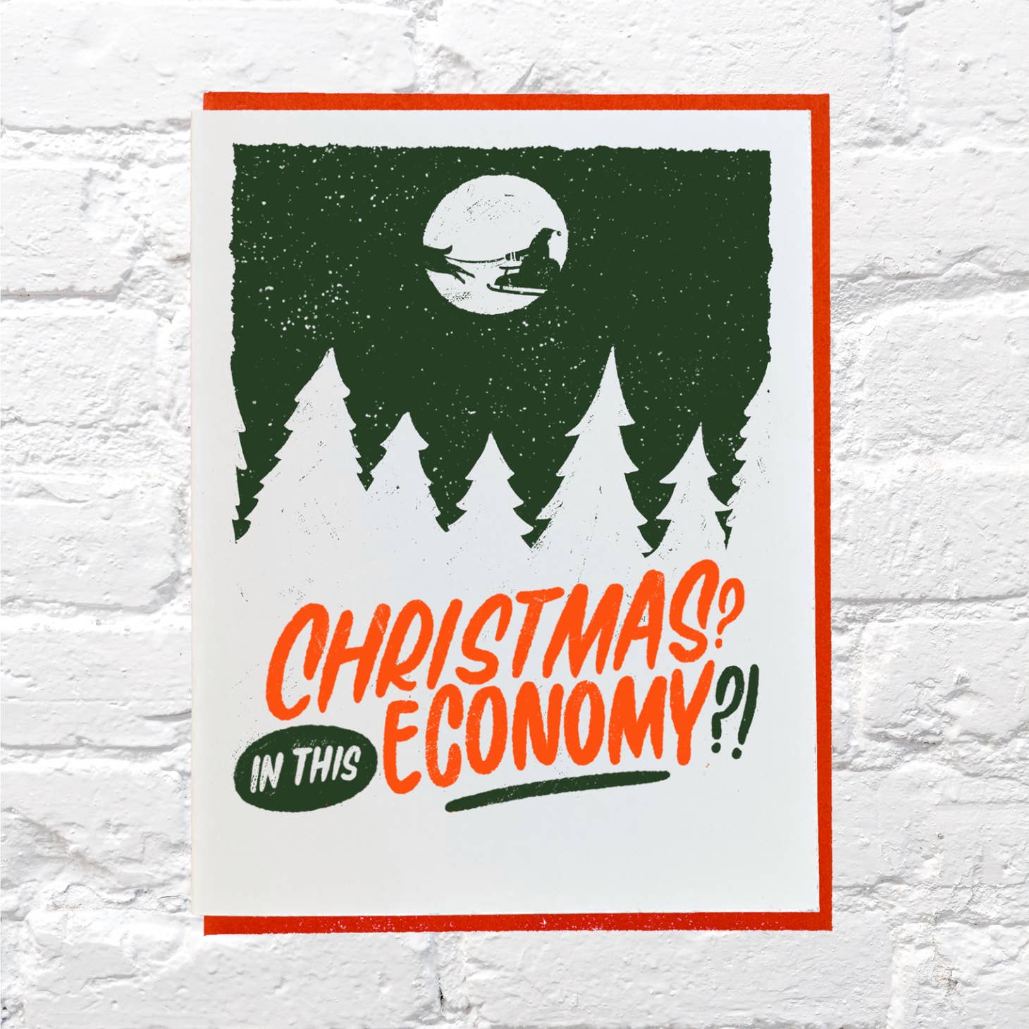 White background with green and white image of Santa and his sleigh in the  moon with red and green text says, "Christmas? In this economy?!" Red envelope is included. 