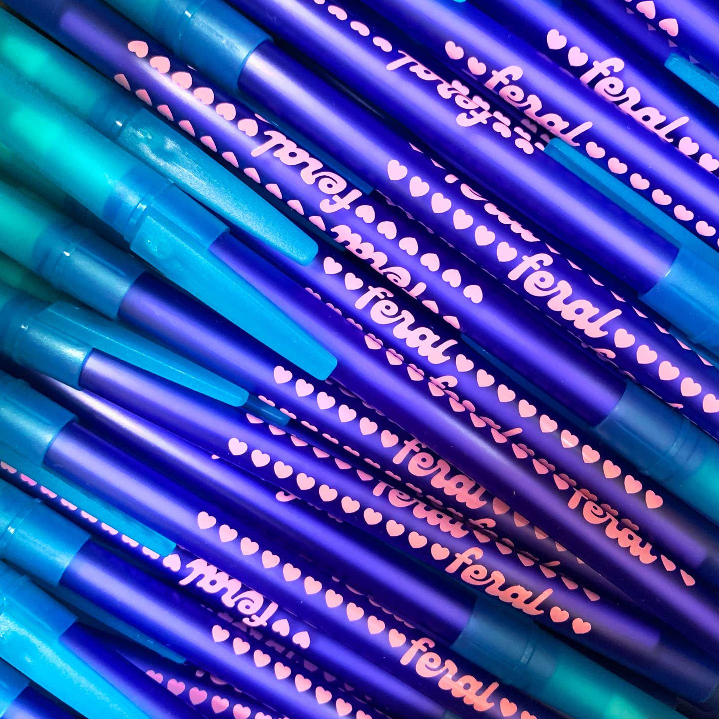 Pen with bright blue barrel and teal cap with pink text says, "feral" with pink hearts. 