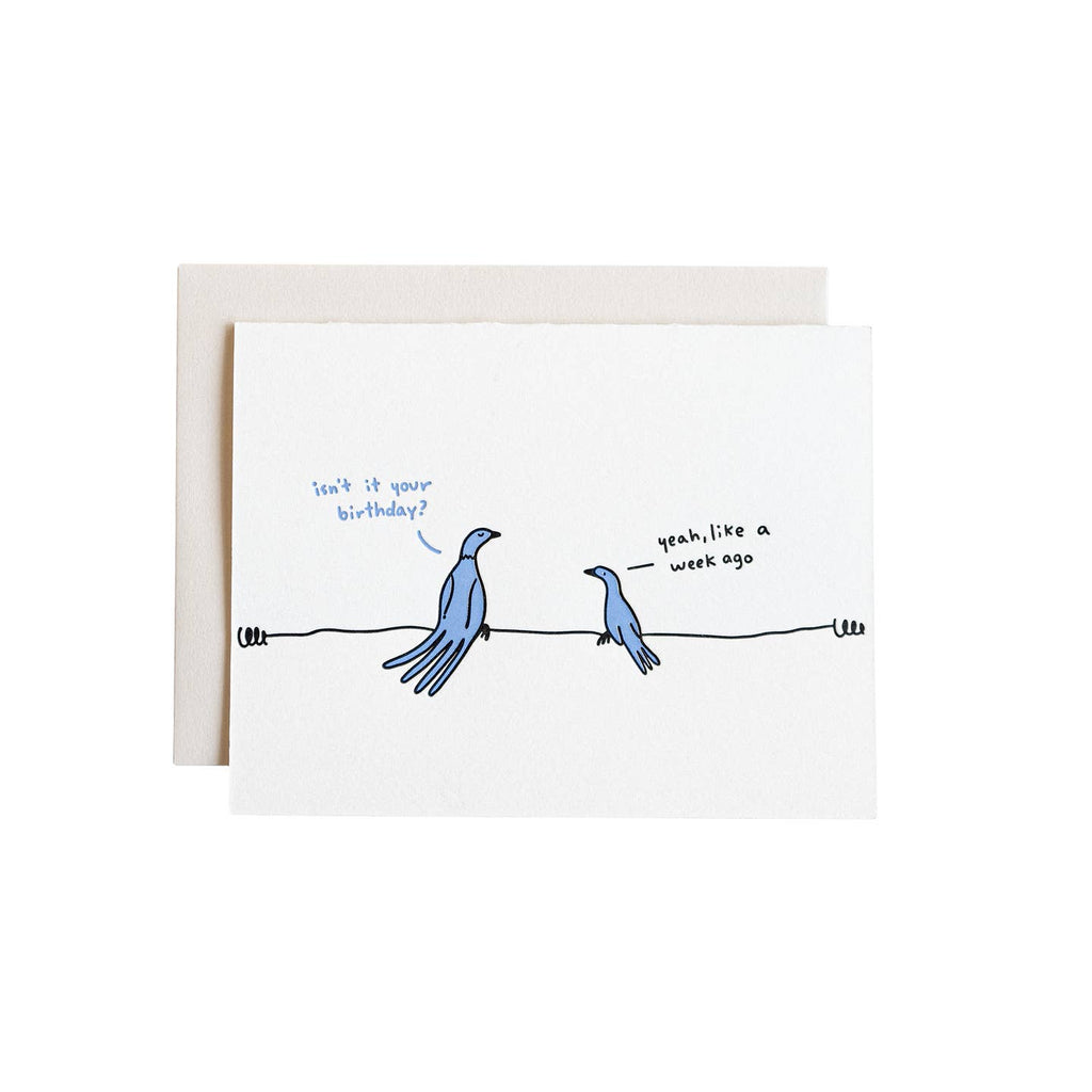 Greeting card with white background and image of two birds sitting on a wire and blue text says, "Isn't it your birthday?" and black text says, "Yeah, like a week ago". Envelope included. 