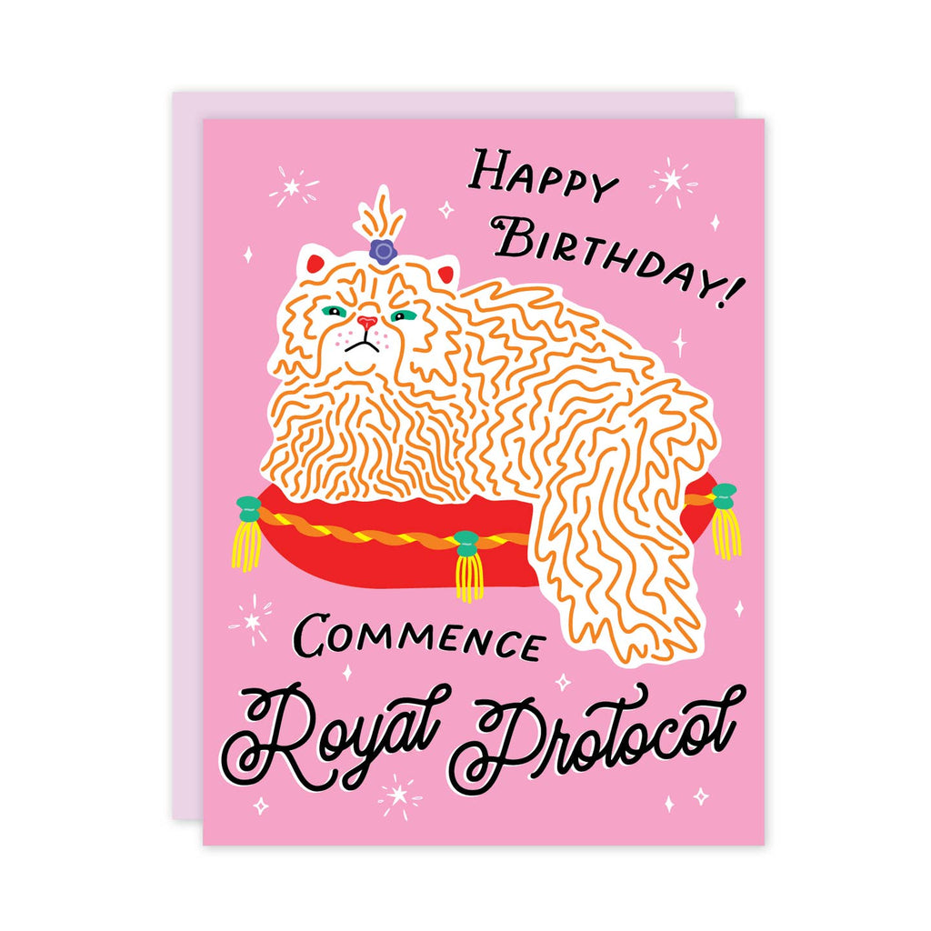 Greeting card with pink background and image of yellow and white cat sitting on red cushion. Black text says, "Happy Birthday!, Commence royal protocol". Lilac envelope included.