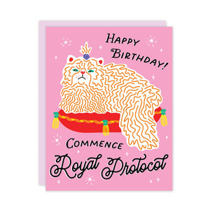 Greeting card with pink background and image of yellow and white cat sitting on red cushion. Black text says, "Happy Birthday!, Commence royal protocol". Lilac envelope included.