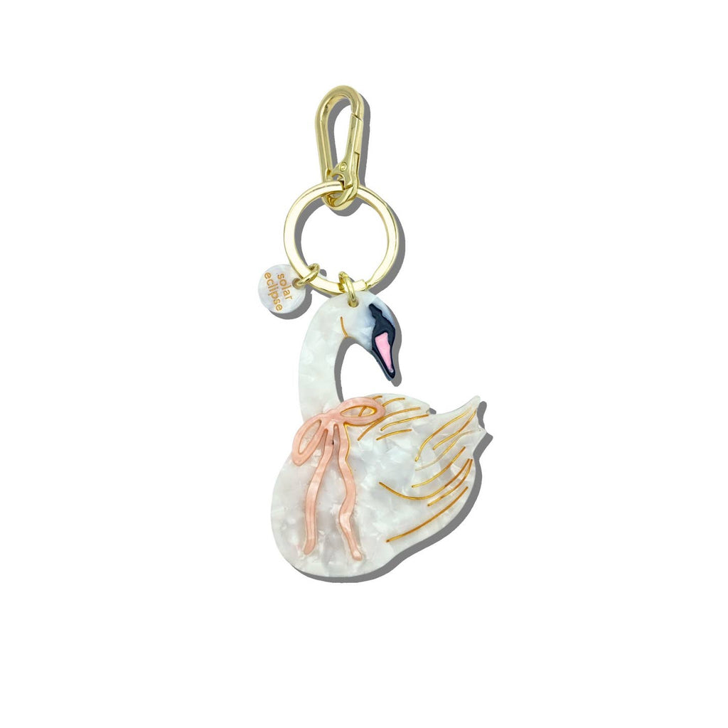 Image of a keychain charm in the shape of a white swan wearing a pink bow around its neck. Gold colored ring and clip. 