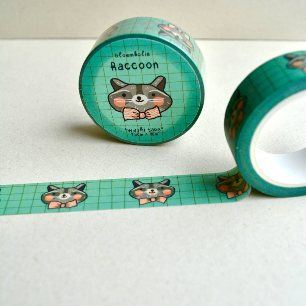 Image of roll of washi tape with green on green grid background and images of a grey, white and black raccoon wearing a pink bowtie. 