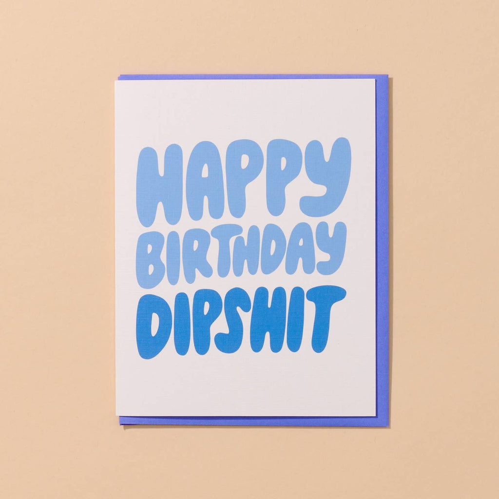 Greeting card with white background  with blue text says, "Happy Birthday Dipshit". Blue envelope included. 