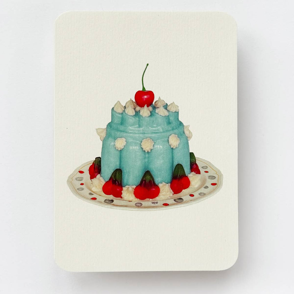 Greeting card with cream background and image of blue Blancmange dessert withj red cherries and white dollops of cream on a ivory plate. Envelope included.