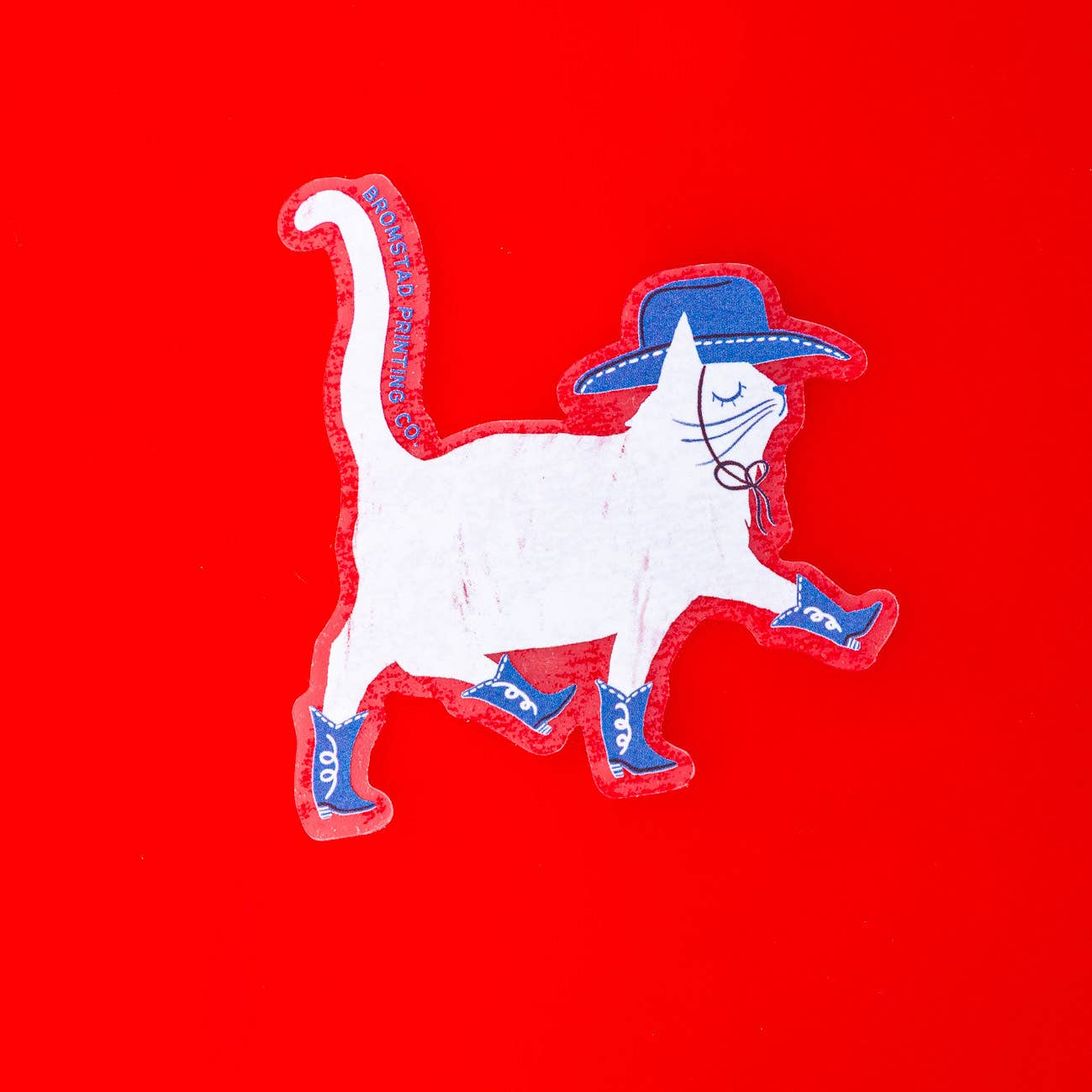Decorative sticker in the image of a white cat wearing blue cowboy hat and boots prancing. 