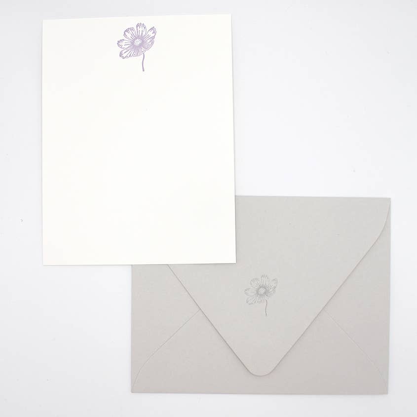 Image of note card with white background and lavender cosmos flower at top of card. Grey envelope with letterpressed flower on back flap. 