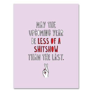 Greeting card with pink background and image of a hand with two fingers crossed. Red and white text says, "May the upcoming year be less of a shitshow than the last.". Envelope included. 