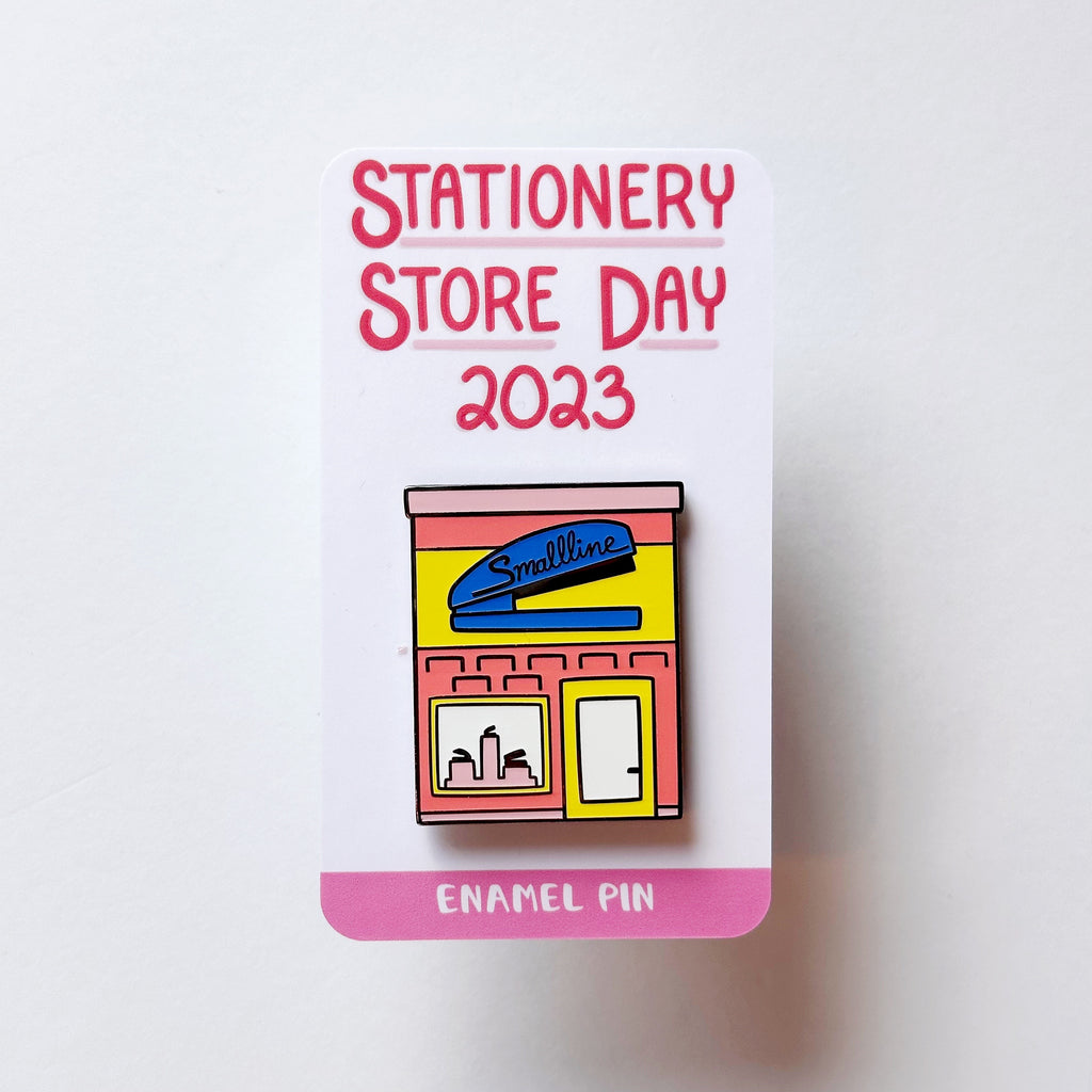 Image of enamel pin of store front with blue stapler with black text says, "Smallline". 