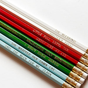 Eight pencils with gold foil text says, "Merry Kiss My Ass Little Full. Lotta Sap. The Blessing! Shitter's Full! Hallelujah! Holy Shit! I Don't Know, Margo! She Wrapped Her Damn Cat Save The Neck For Me, Clark".