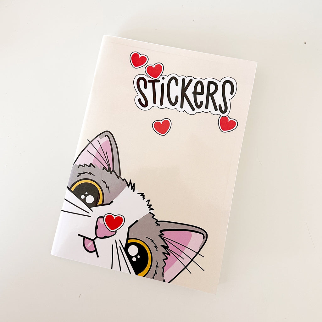 Image of notebook with cream background and image of grey and white kitty with a red heart sticker stuck on its nose. Black text says "Stickers". 