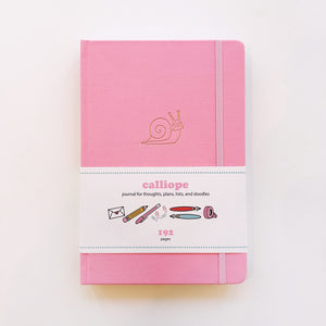Image of pink journal with image of gold foil snail and pink elastic strap on right side to hold closed. 