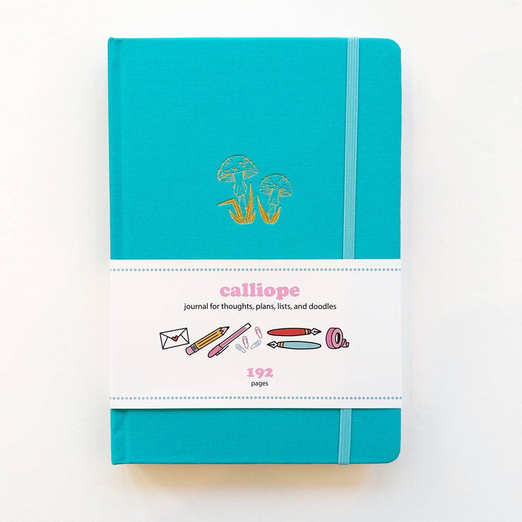 Image of journal with teal background and gold foil image of twin mushrooms with elastic holder on right side. 