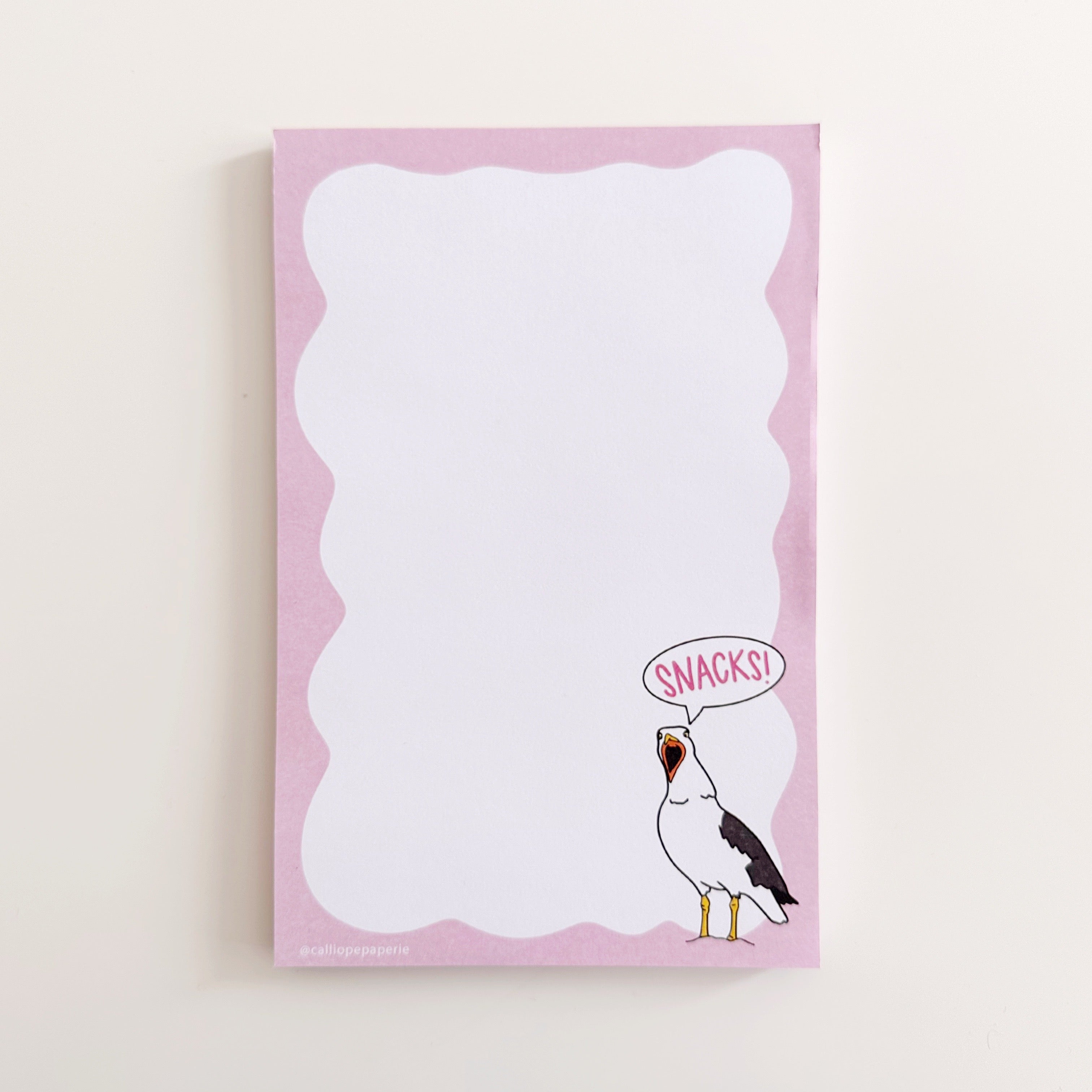 Notepad with white background and pink wavy border with image of a black and white seagull screaming in the bottom right corner with word bubble with pink text says, "Snacks!". 