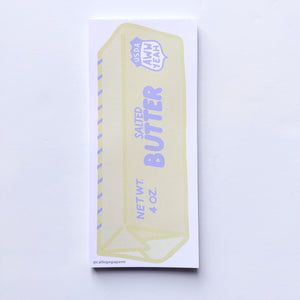 Notepad with image of stick of yellow butter with pale blue text says, "Salted butter, Net wt 4 oz., USDA Aww yeah" with blue markings for tablespoons with white border. 