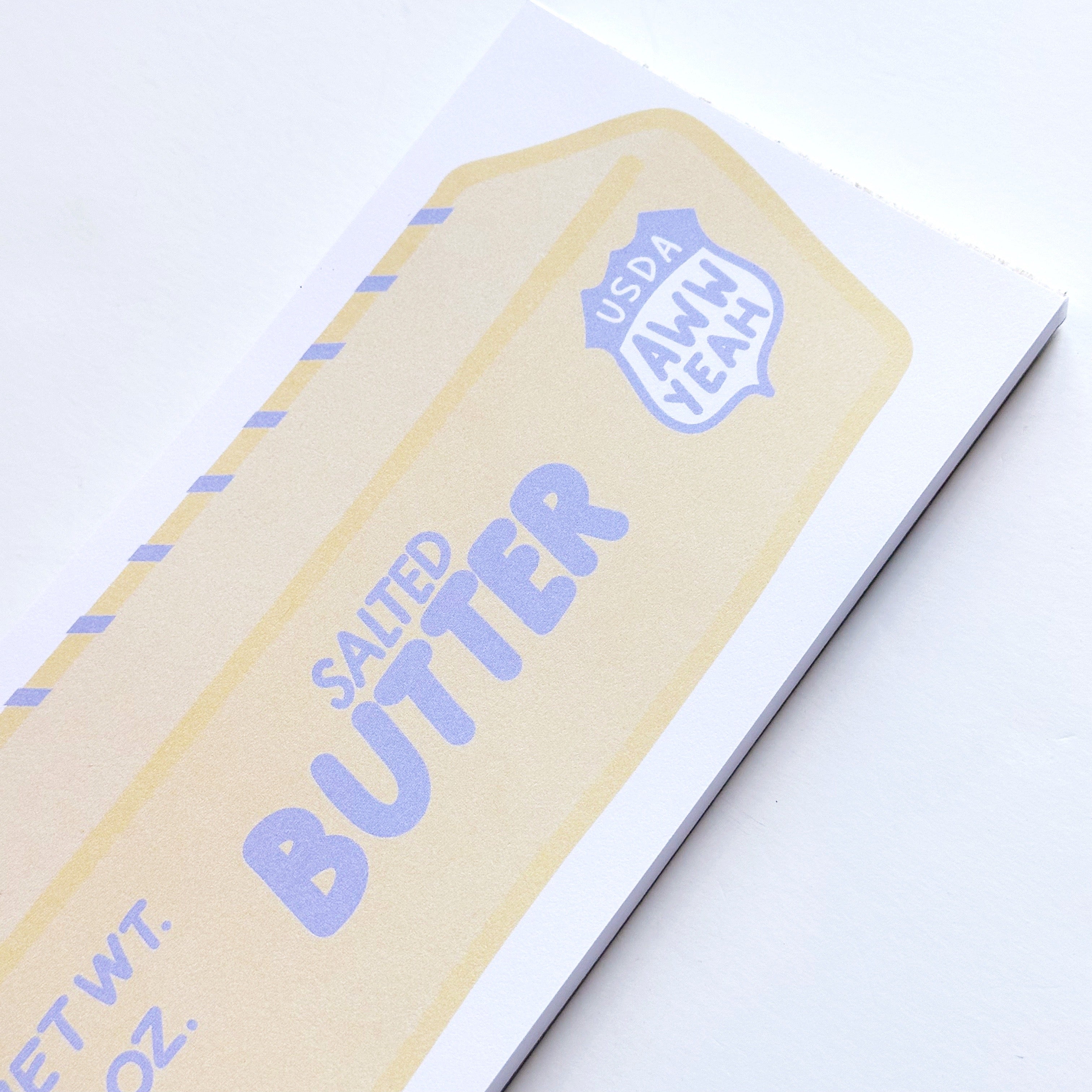 Notepad with image of stick of yellow butter with pale blue text says, "Salted butter, Net wt 4 oz., USDA Aww yeah" with blue markings for tablespoons with white border. 