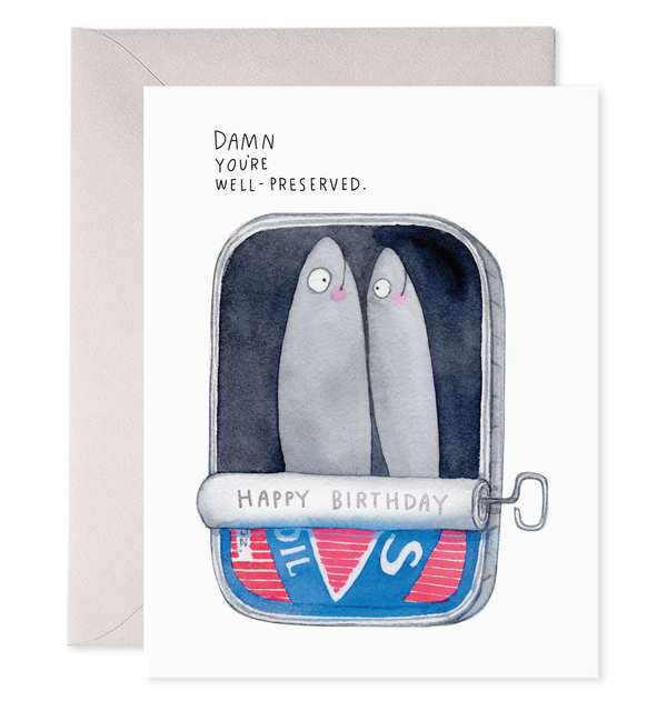 Greeting card with white background with image of an open can containing two grey sardines with black text says, "Damn You're well preserved." and grey text says, "Happy birthday" on the rolled back can key. Grey envelope included. 