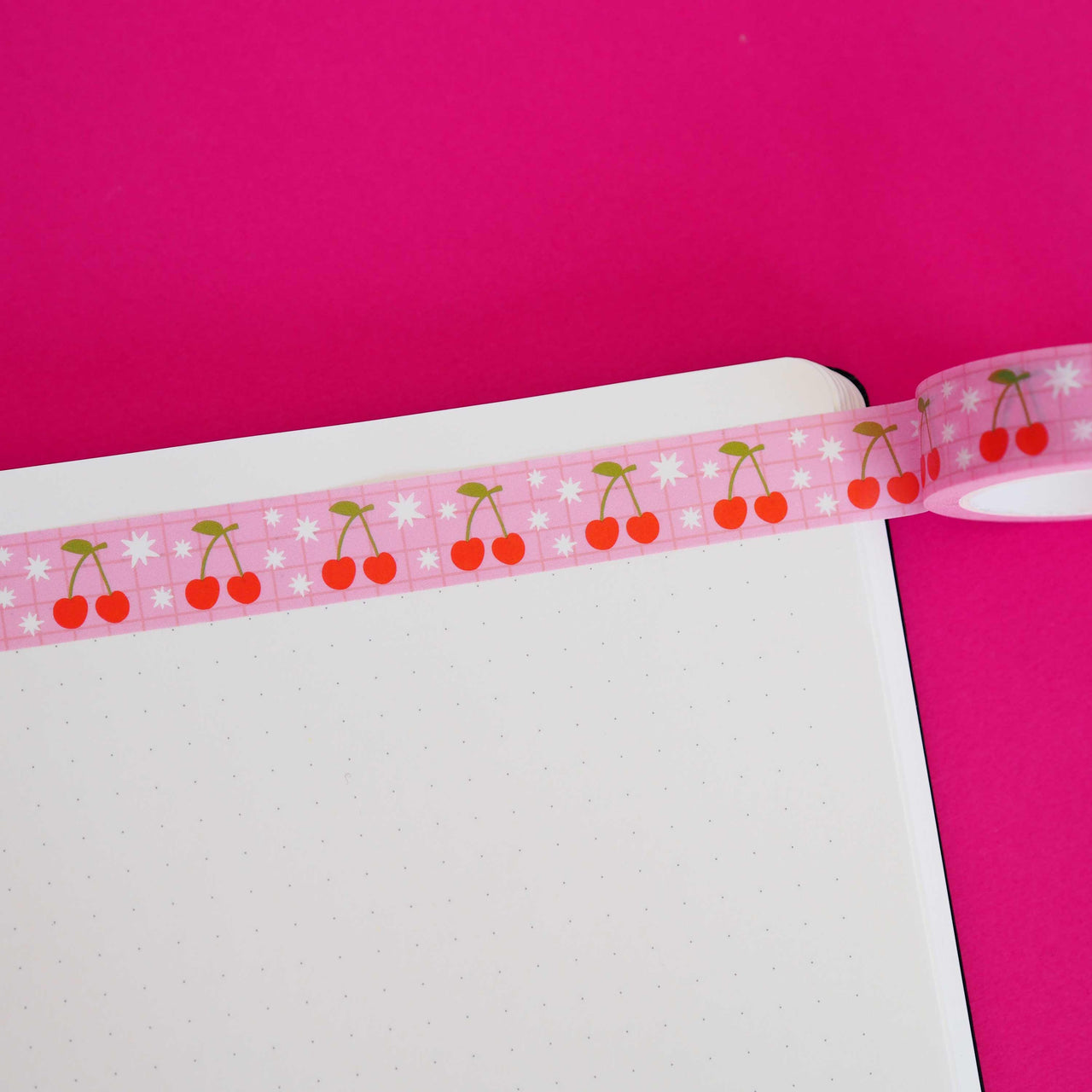 Washi tape with pink background and images of red cherries with green stems and leaves and white bursts.