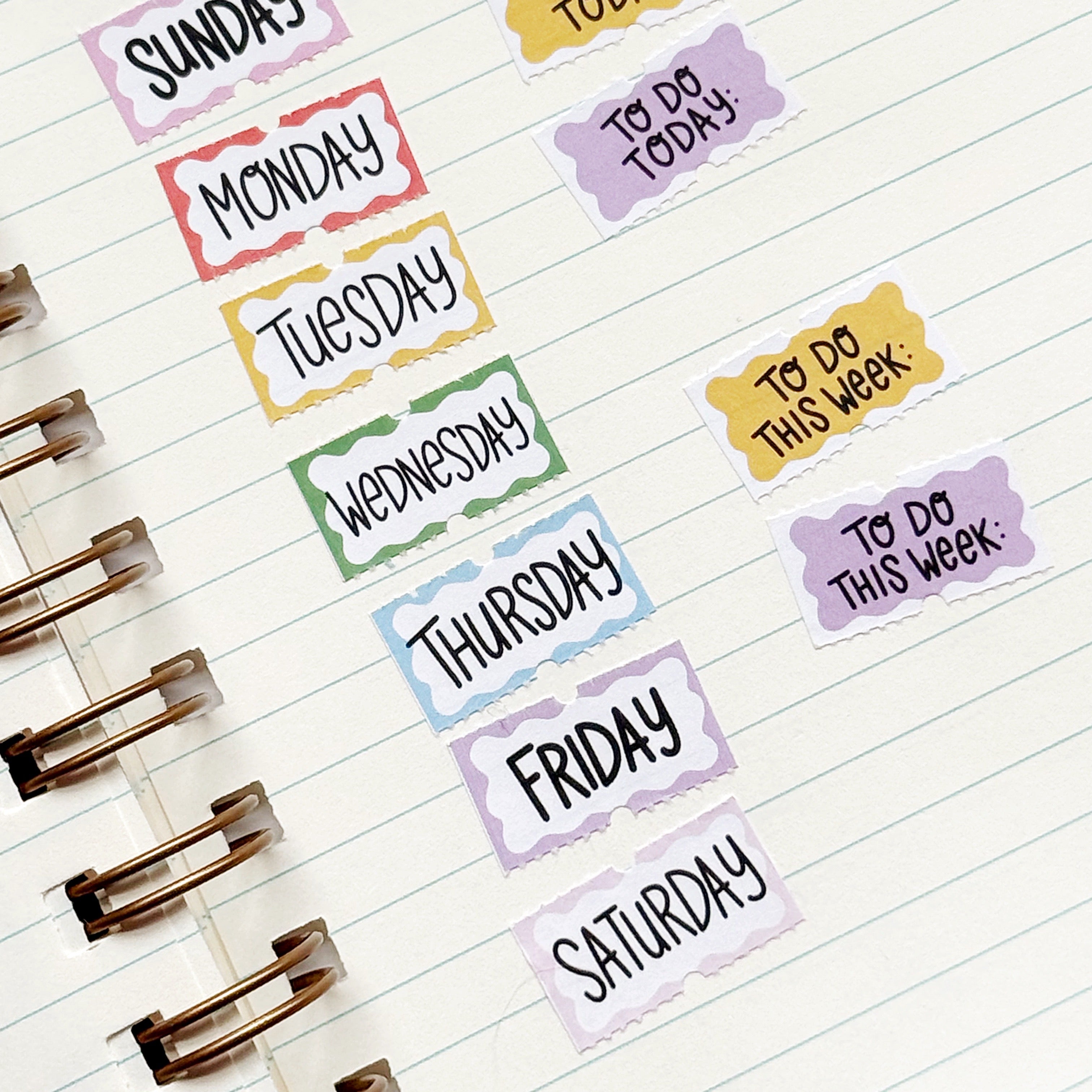 Small stickers with yellow, pink, white, blue backgrounds and black text says, "Sunday, Monday, Tuesday, Wednesday, Thursday, Friday, Saturday, To Do today, To do this week, Month".