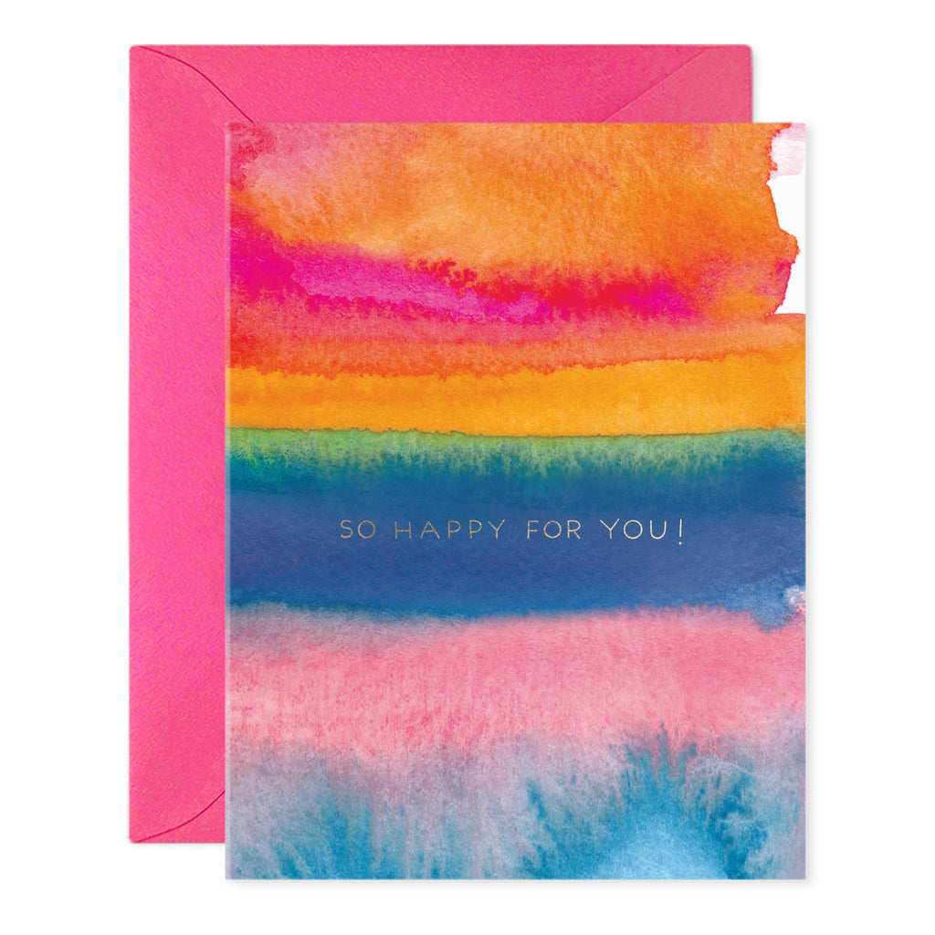 Greeting card with rainbow watercolor style background and gold text says, "So happy for you!". Hot pink envelope included. 