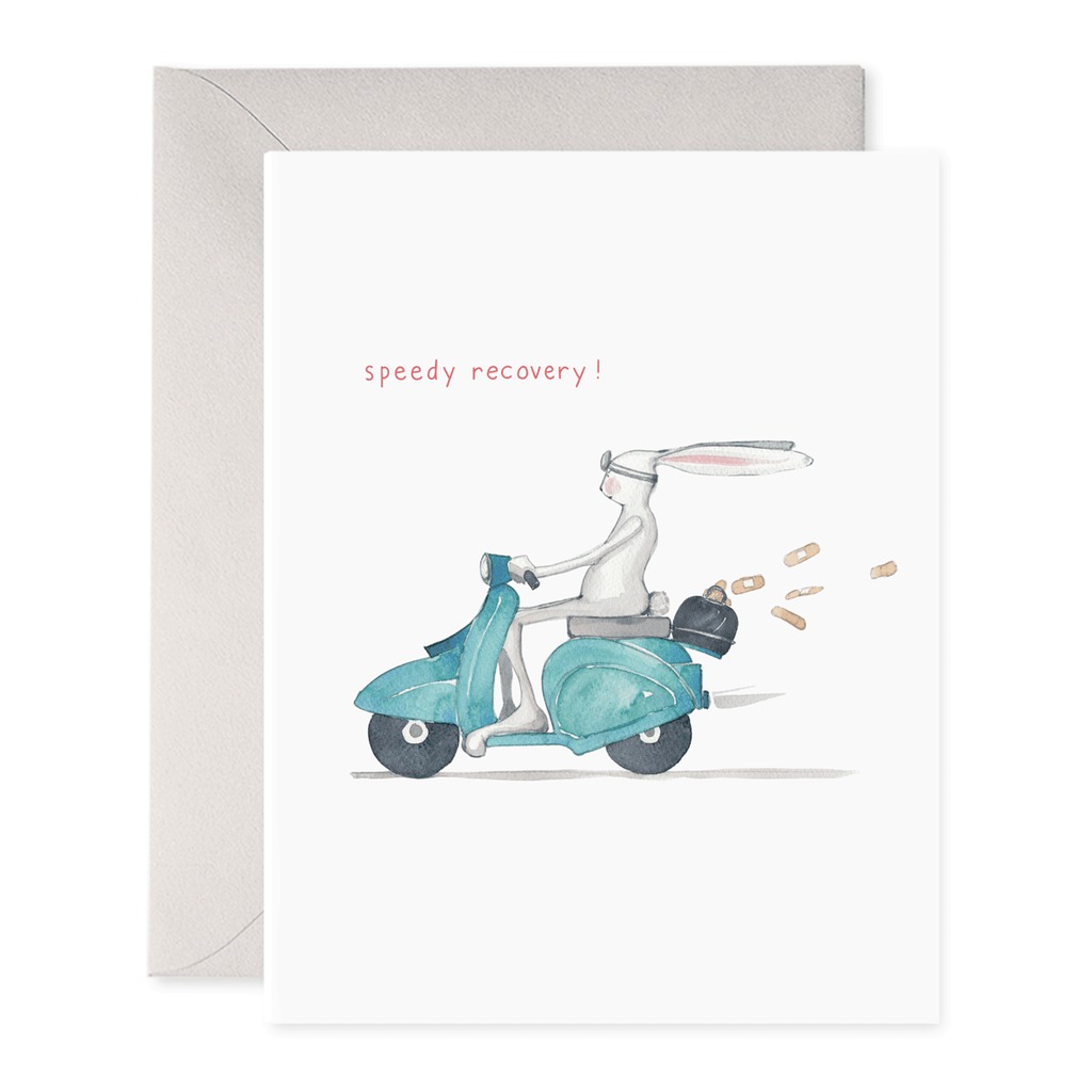 Greeting card with white background with image of a white rabbit riding a blue moped sixth a medical bag on the back with bandaids flying out of it. Red text says, "speedy recovery". Grey envelope included. 