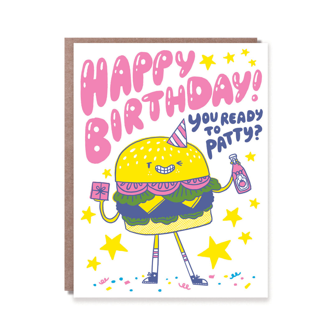 Greeting card with white background and image of a burger wearing a party hat and holding a gift and bottle of ketchup. Pink and blue text says, "Happy Birthday, you ready to patty?". Kraft envelope included.