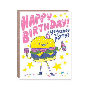 Greeting card with white background and image of a burger wearing a party hat and holding a gift and bottle of ketchup. Pink and blue text says, "Happy Birthday, you ready to patty?". Kraft envelope included.