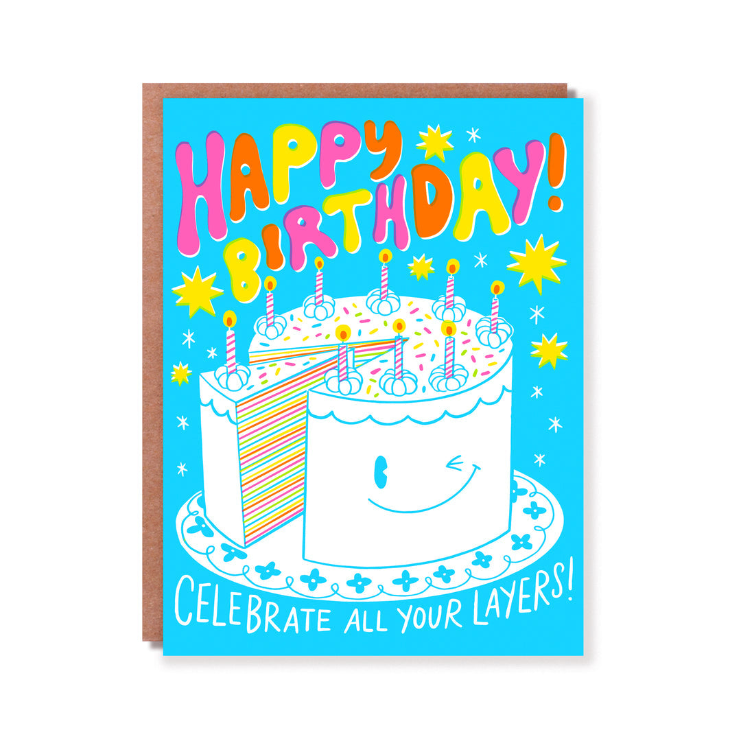 Greeting card with blue background and image of a layer Birthday cake with candles. Pink, orange and yellow text says, "Happy Birthday!" and white text says, "Celebrate all your layers!". Kraft envelope included. 