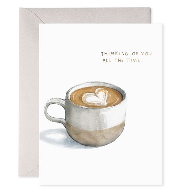 Greeting card with white background and image of cup of coffee with white heart shaped foam. Grey text says, "Think of you all the time". Grey envelope included. 