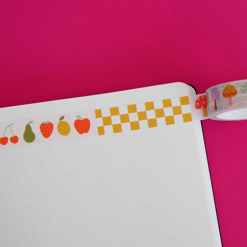 Washi tape with patterns of mustard and white checkerboard, fruits including cherries, pear, strawberry, lemon and apple and toadstools in red, green, pink, and lilac.