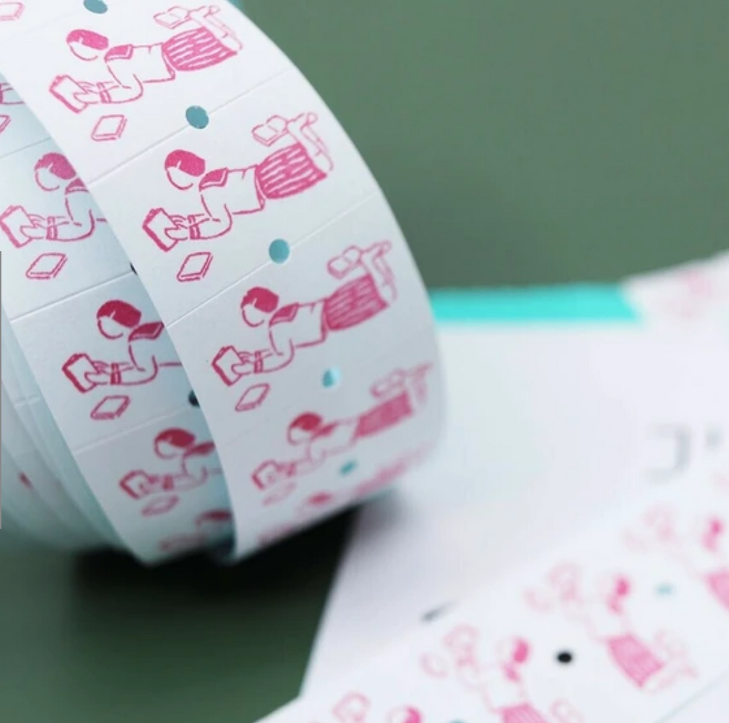 Label sticker roll with white background and red image of a person lying down and reading a book.
