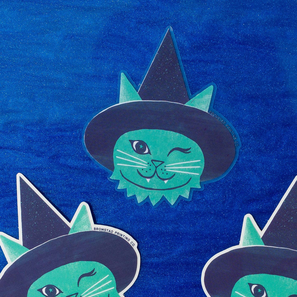 Decorative sticker with image of a green cat winking and wearing a dark blue witch hat. 