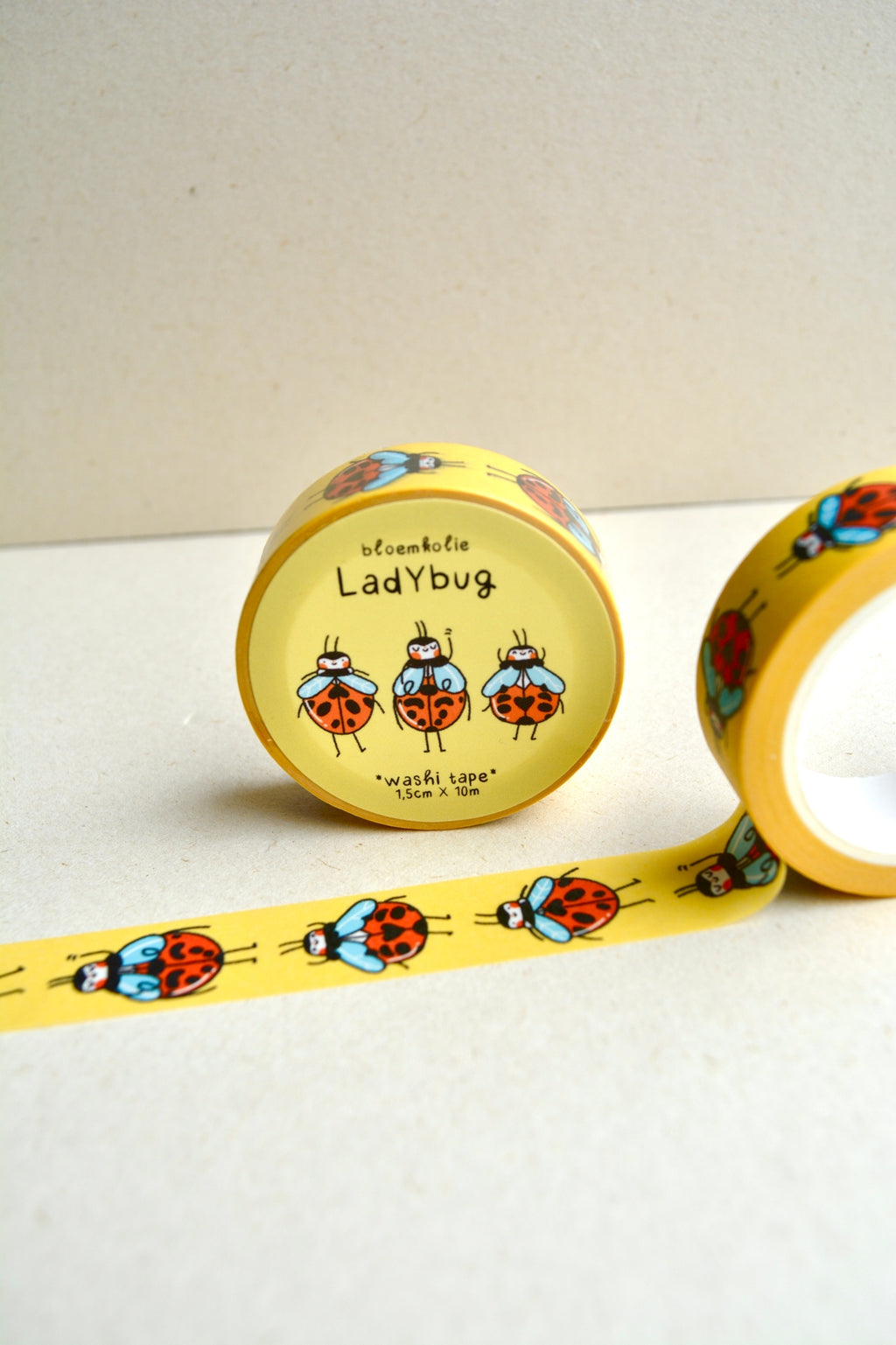 Image of roll of washi tape with yellow background and images of red and black ladybugs with blue collar. 
