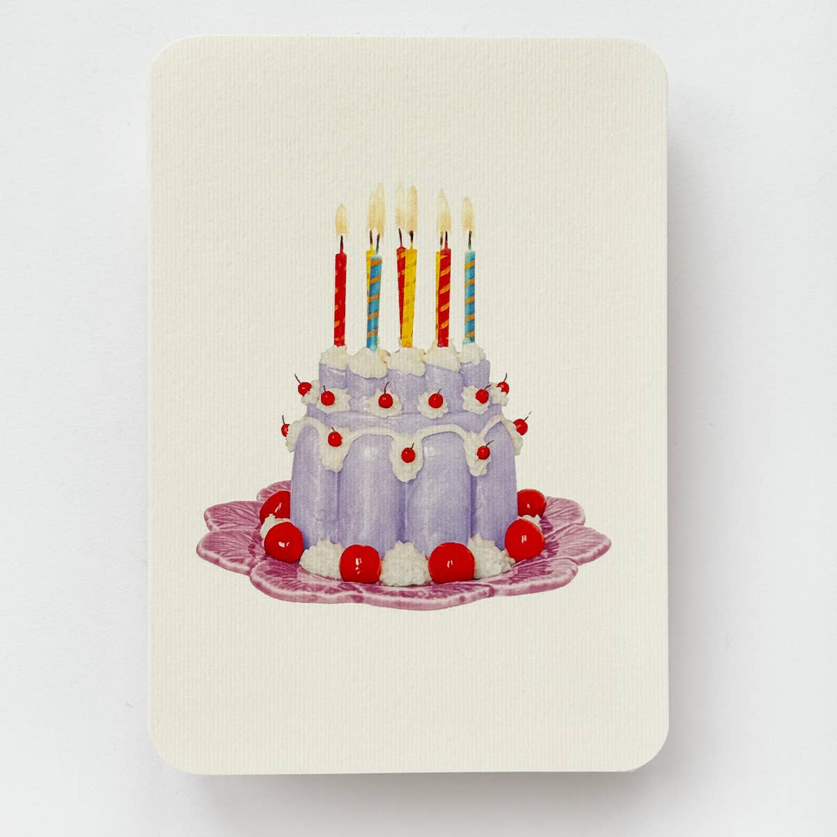 Greeting card with cream background and image of lavender Blancmange dessert with lit candles on top. Envelope included.