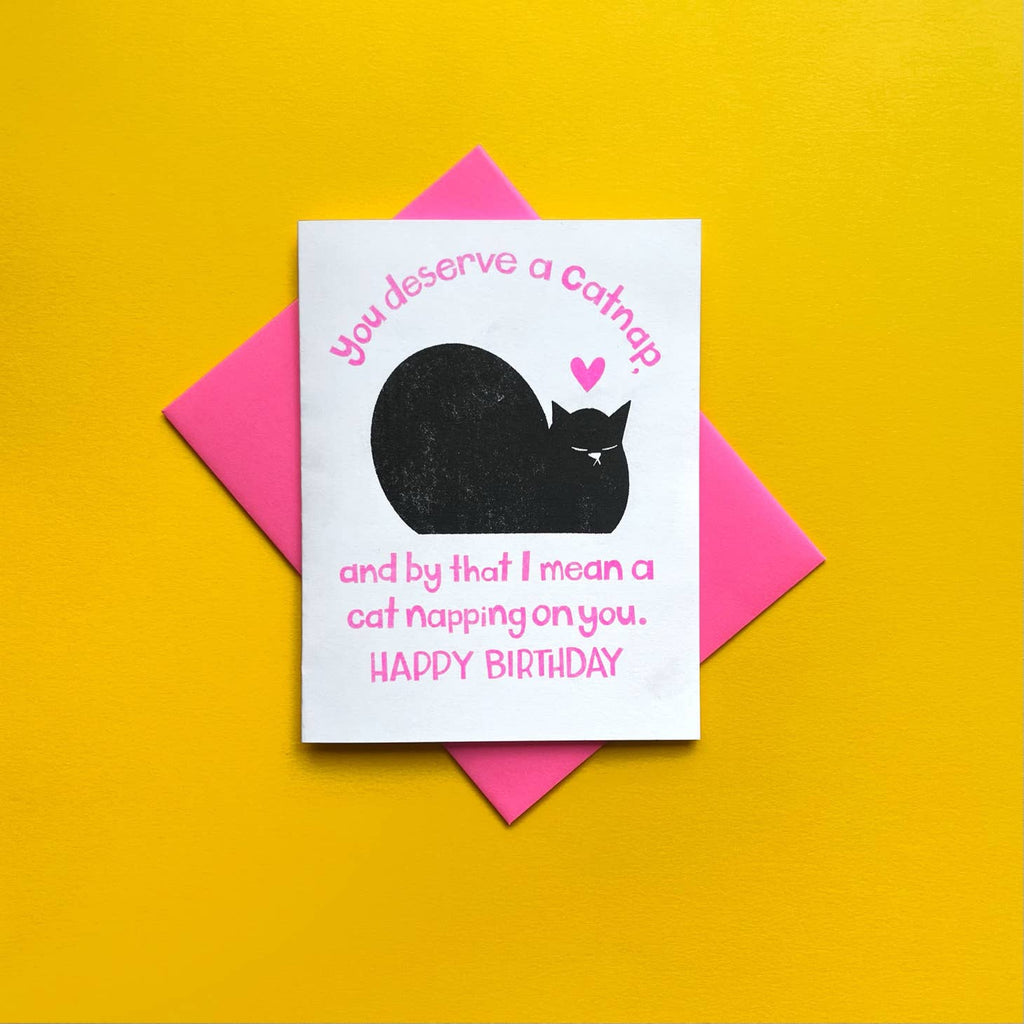 Greeting card with white background and image of black cat napping with a pink heart over its head. Neon pink text says, "You deserve a cat nap. And by that I means a cat napping on you. Happy Birthday". Bright pink envelope included. 