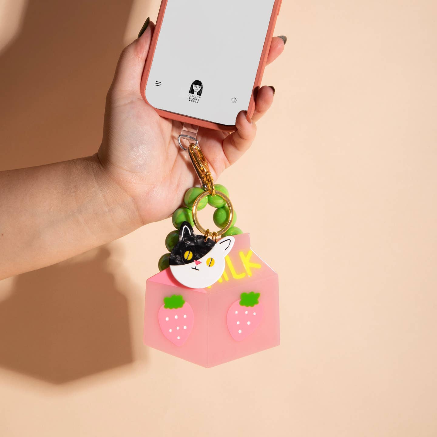 Image of cat and milk charm hanging on a charger port on phone. 