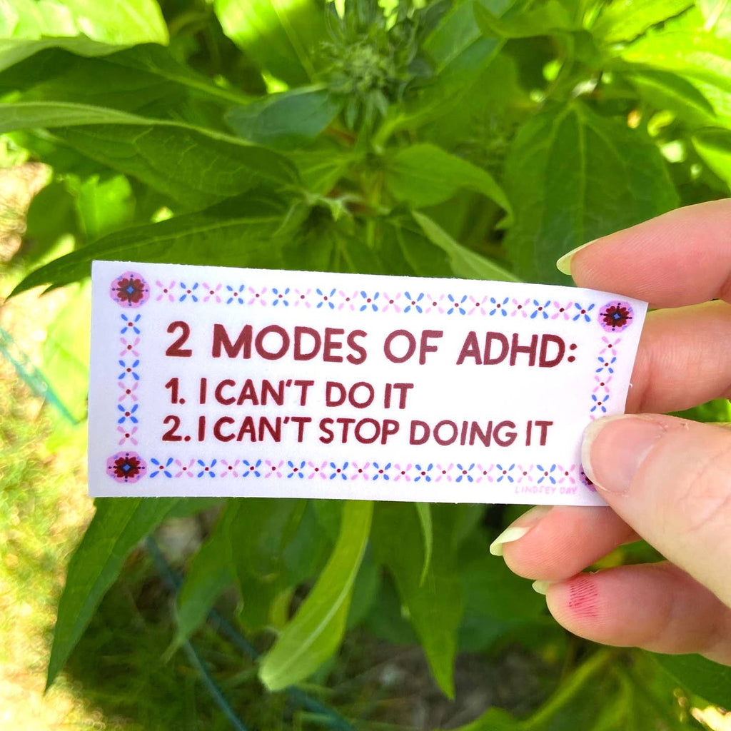 Image of sticker with white background with burgundy text says, "2  modes of ADHD: 1. I can't do it, 2. I can't stop doing it". Border of pink and blue x's. 