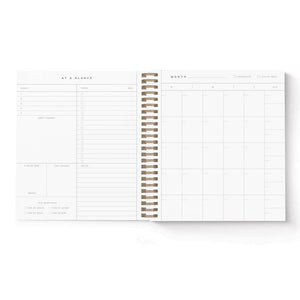 Planner pages with white background and left side has columns and lines with black text, "At a glance" and "goals, tasks, don't forget, milestones, notes". Right page has white background with black text, "month" with grid for months and dates. 