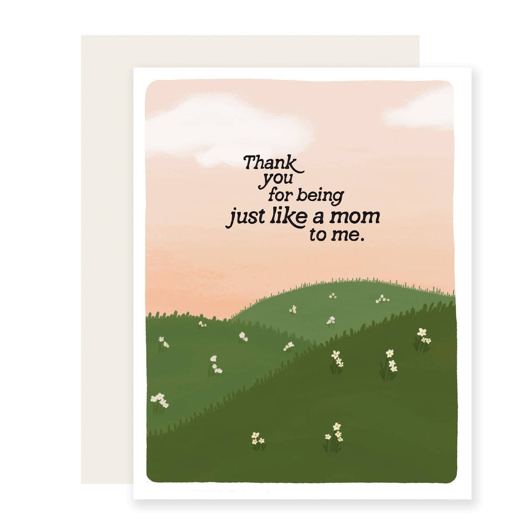 Greeting card with pink background with white clouds and green hills with black text says, "Thank you for being just like a mom to me. " Cream envelope included.