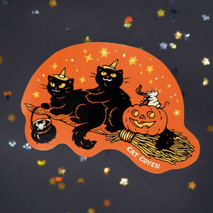 Decorative sticker with orange background with image of two black cats and a pumpkin riding on a broom.